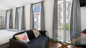 Une chambre d’hôtel moderne équipée d’un lit, d’un canapé, d’une table en verre et de grandes fenêtres avec des rideaux.