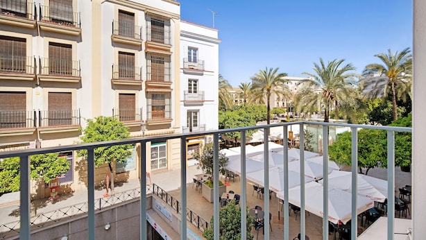 Un immeuble à plusieurs étages doté de balcons, une cour avec des espaces de détente en plein air et des palmiers.