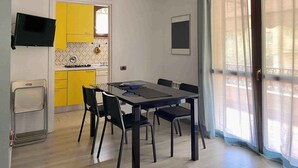 Een knus woongedeelte met een eethoek, een kitchenette en een groot raam voorzien van gordijnen.