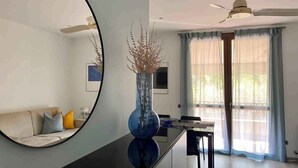 Een moderne woonkamer met een grote spiegel, een eethoek met een tafel en stoelen, een plafondventilator en uitzicht op de omgeving door grote ramen.