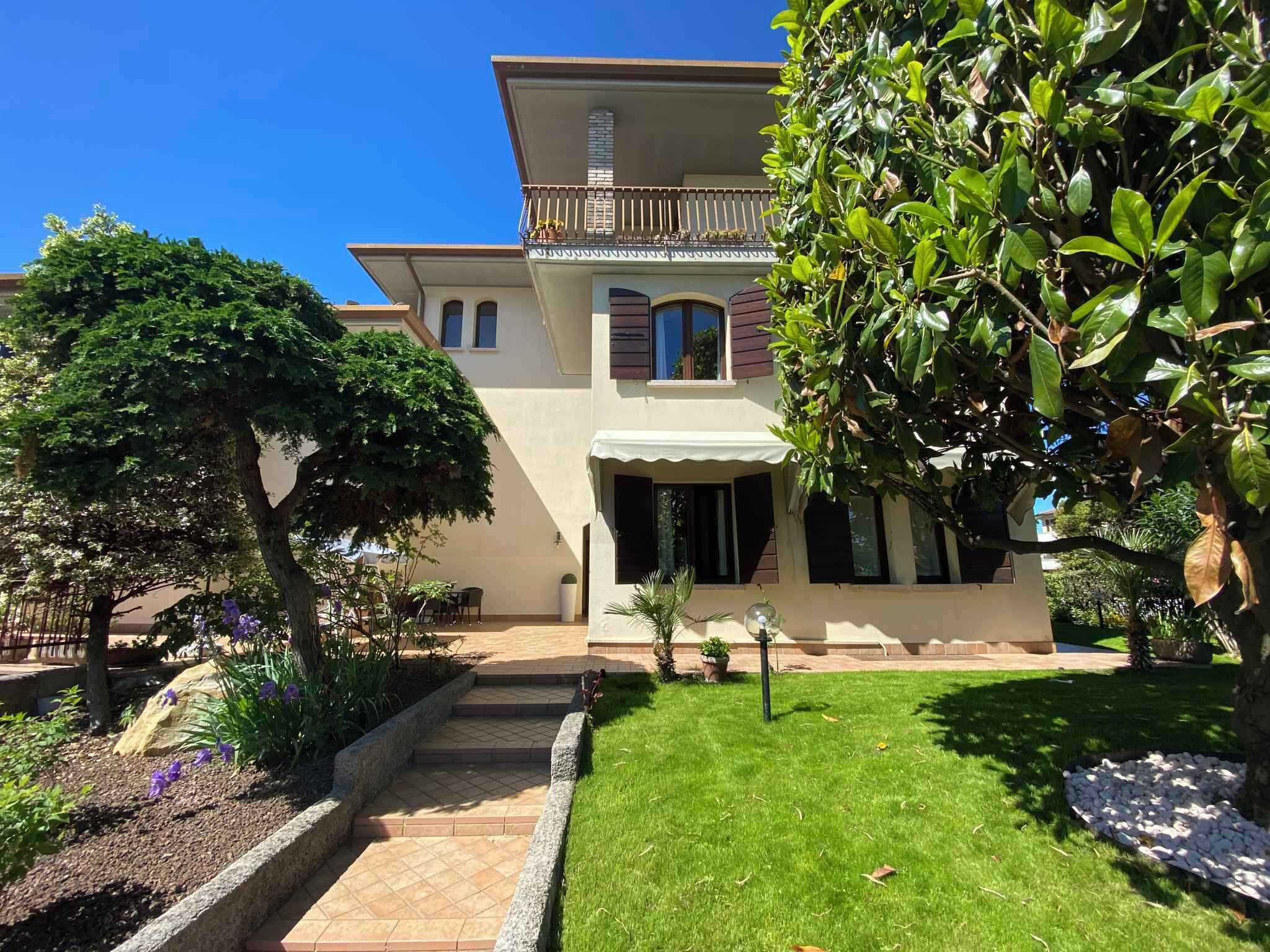 Une maison à deux étages avec un balcon, un jardin avec une pelouse et un chemin menant à l’entrée.