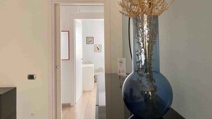 Een hal met een modern interieur, een grote blauwe vaas met gedroogde planten, en een deur die naar een badkamer leidt.
