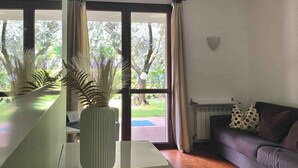 Ein Wohnzimmer mit einer Couch, einem Couchtisch und Blick auf einen Garten durch große Fenster.