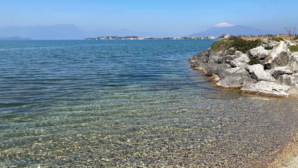 Una vista despejada del litoral, con costa rocosa, mar tranquilo y edificios lejanos en una península.