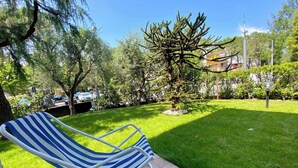 Un jardín con una silla de descanso a rayas, un árbol pequeño y una zona pavimentada.