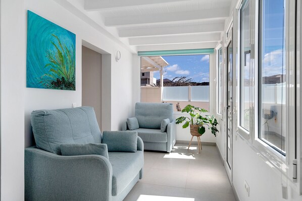 A modern living room with two grey sofas, a large window with a view, and a painting on the wall.