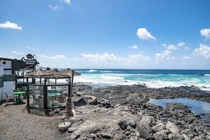 A beachside restaurant with outdoor seating, a glass enclosure, and a view of the ocean.