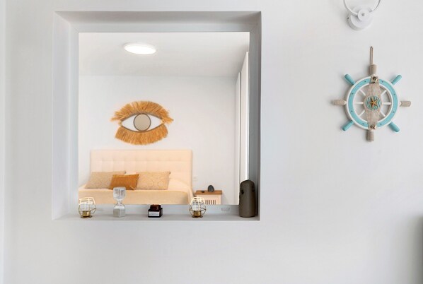 A bedroom with a bed, a wall-mounted eye decoration, a ship's wheel, and bedside tables with items.