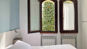 Ein Schlafzimmer mit Bett, Nachttisch, Fenster und Blick ins Grüne sowie einer Heizung.
