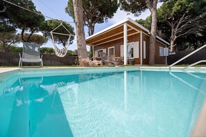 En swimmingpool med liggestole og en træbygning i baggrunden.
