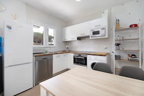 Et moderne køkken med hvide skabe, rustfrie hvidevarer, en træbordplade og et spiseområde.