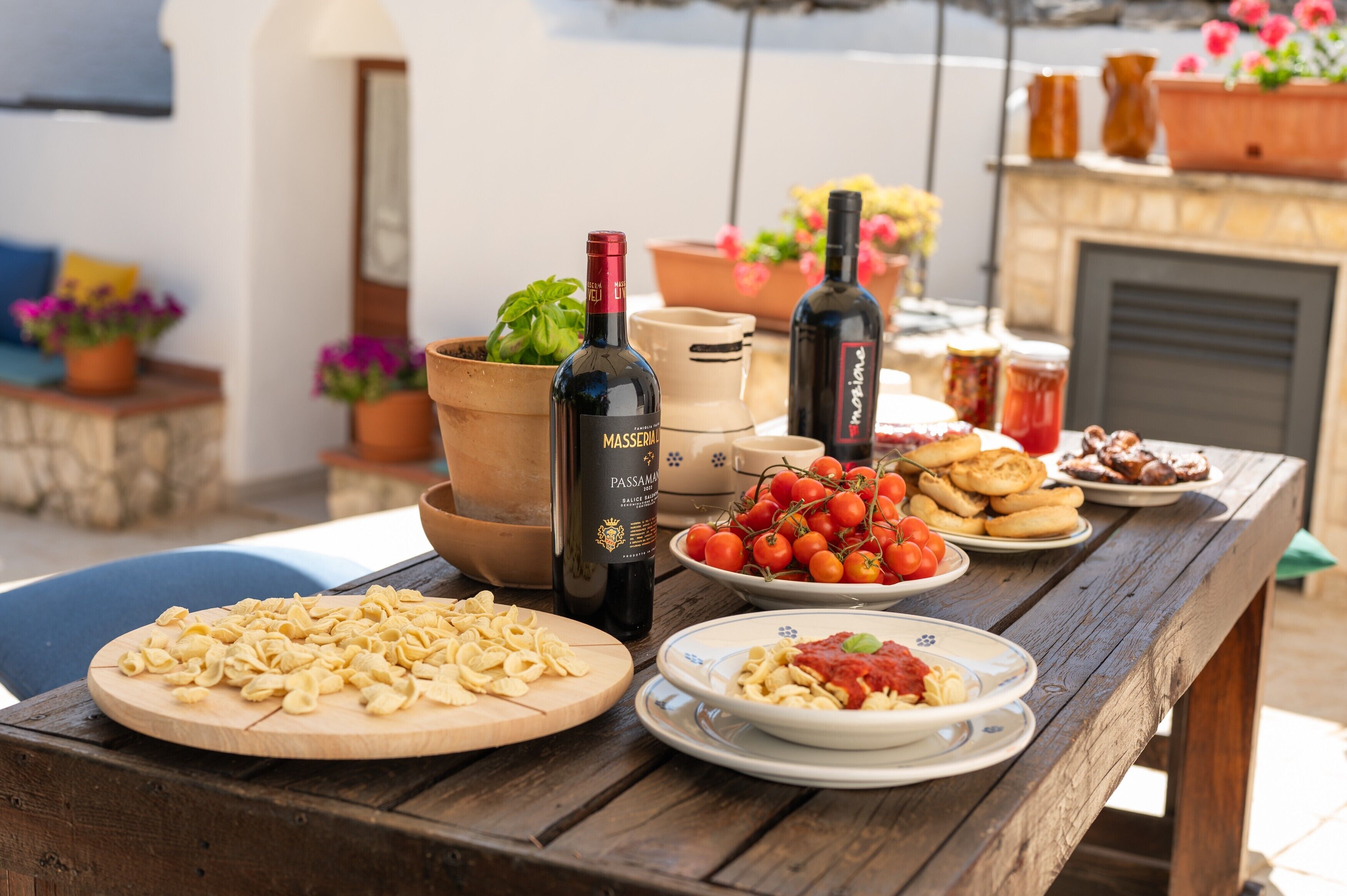 A wooden table with food, wine bottles, and potted plants.