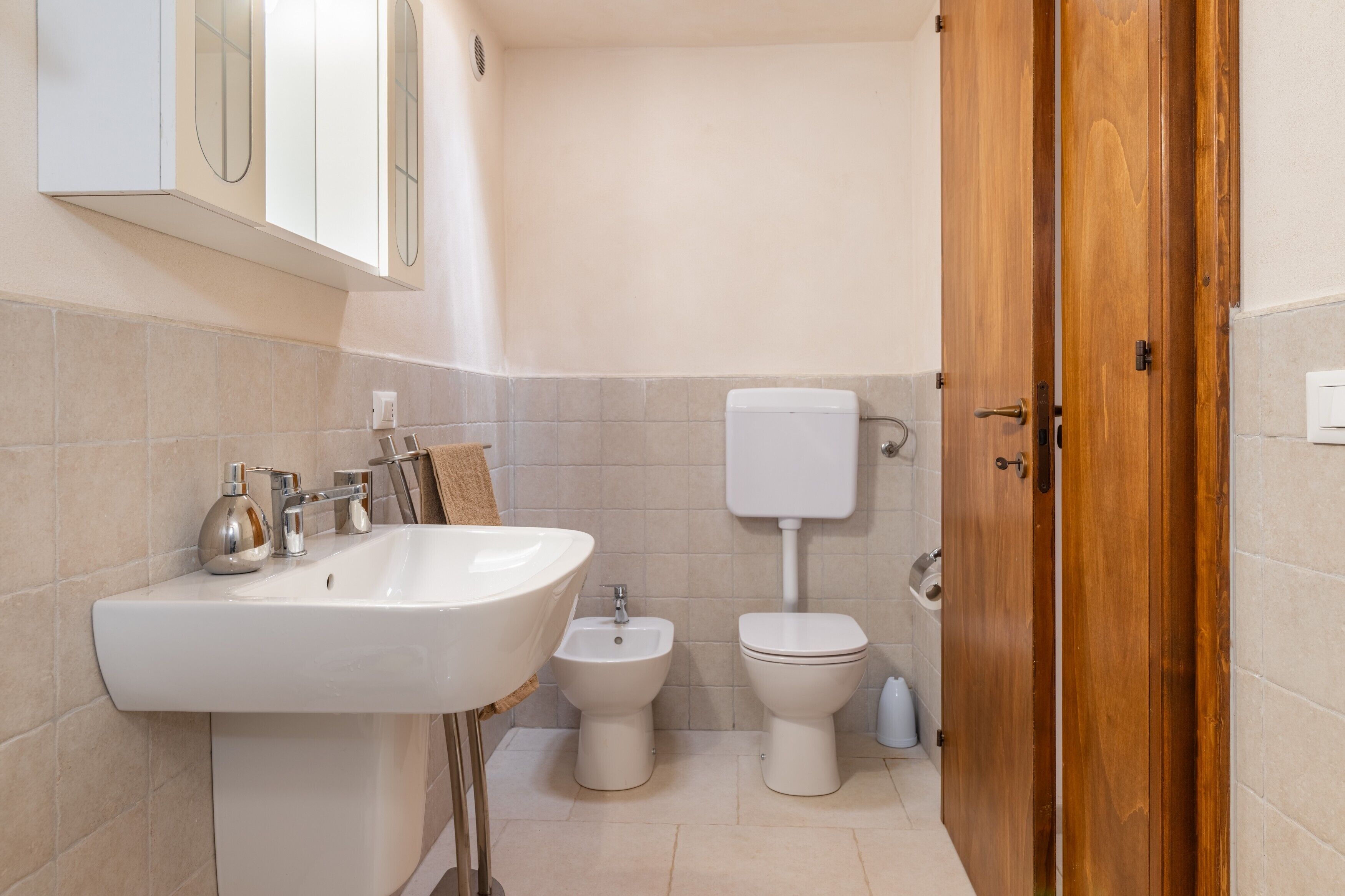 A bathroom with a sink, bidet, toilet, and wooden door.
