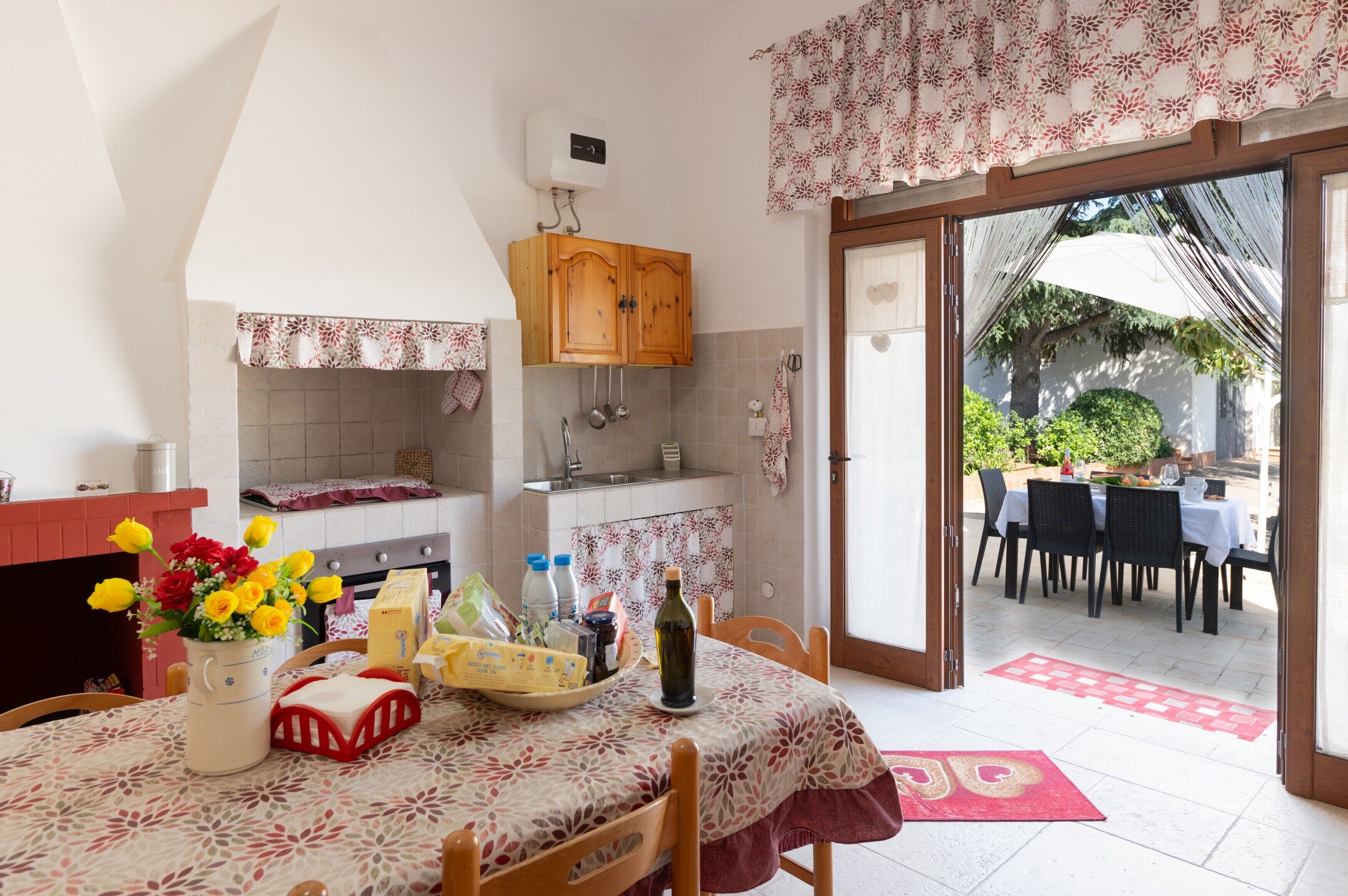 A kitchen with a dining area, a table with a floral tablecloth, and a view of the outside.