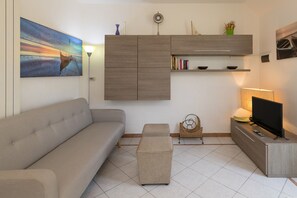 Un salon moderne comprenant un canapé, un pouf, un meuble pour la télévision et des étagères murales.