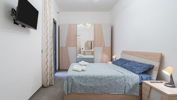 A modern bedroom with a bed, bedside table, lamp, and a TV mounted on the wall. - Apartment "Erre House" with Private Terrace & Wi-Fi (Avola)