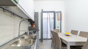 A modern kitchen with stainless steel sinks, a built-in oven, and a dining area with a table and chairs. - Apartment "Erre House" with Private Terrace & Wi-Fi (Avola)