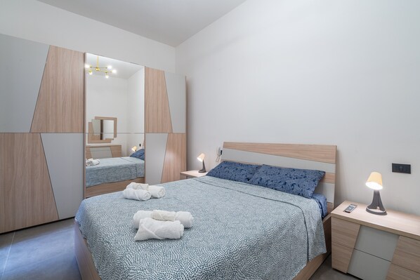 A modern bedroom with a bed, bedside tables, a mirror, and a lamp.