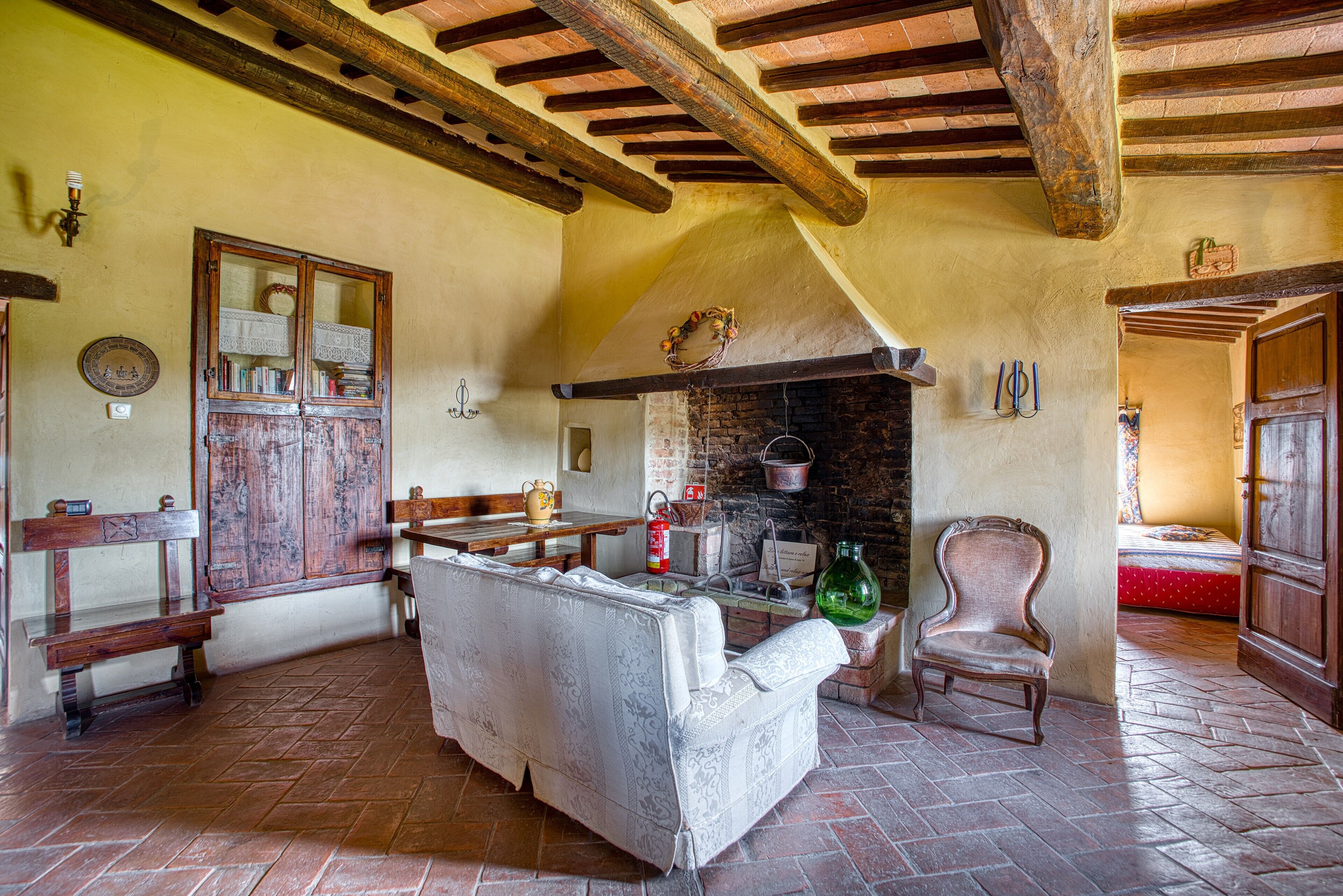A rustic room with exposed wooden beams, a fireplace, a bench, a sofa, and a chair.