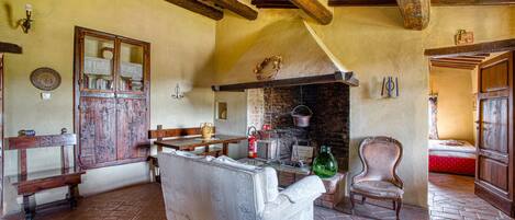 A rustic room with exposed wooden beams, a fireplace, a bench, a sofa, and a chair.