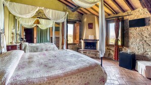 A room with a bed, a fireplace, a television, and a stone wall. - Villa 'Le Buccole Country House' con vista sulle colline perugine, Wi-Fi e aria condizionata. (Marsciano)