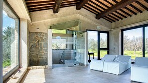 A modern interior with a stone wall, glass door leading to a kitchen, and a white sofa with a view of greenery. - Villa 'Le Buccole Country House' con vista sulle colline perugine, Wi-Fi e aria condizionata. (Marsciano)