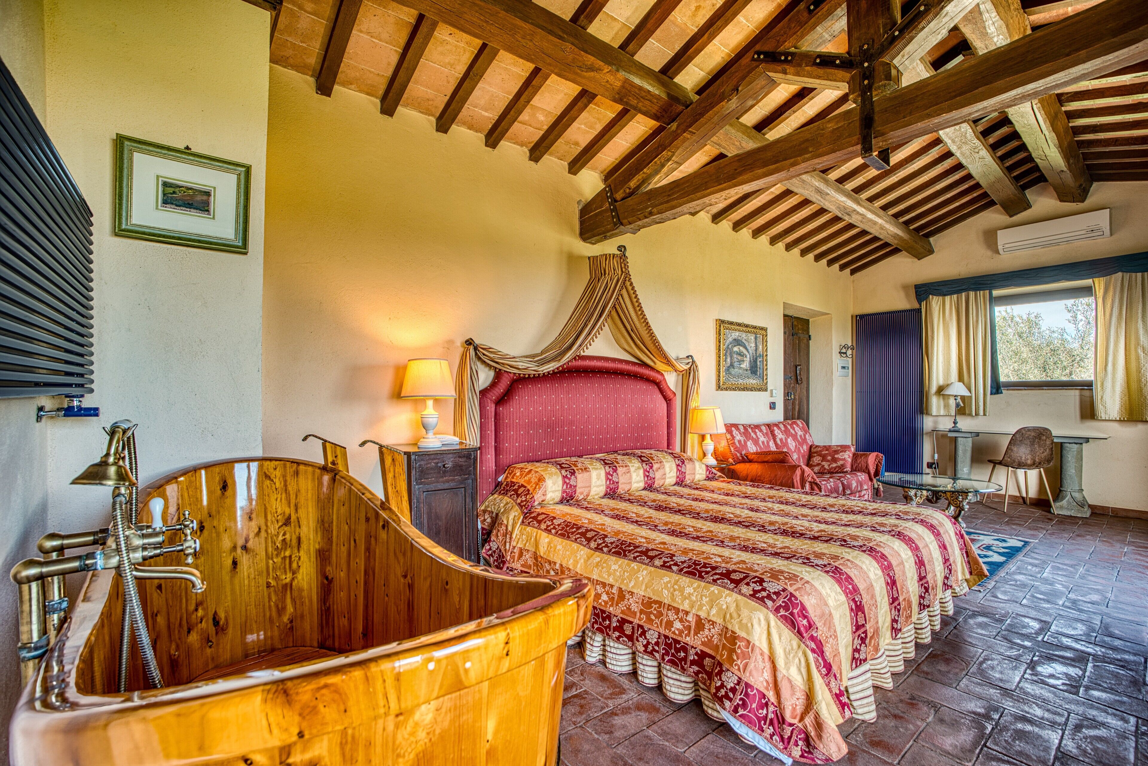 A bedroom with a large wooden bathtub, a four-poster bed, and a stone floor.