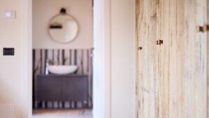 A hallway leading to a bathroom with a round mirror, a sink, and striped towels.