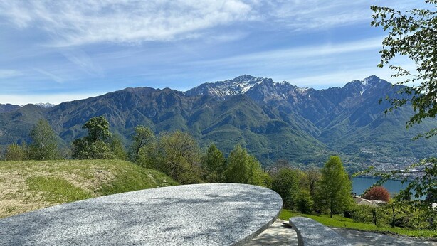 A stone bench overlooking a mountainous landscape with a lake and buildings in the distance.