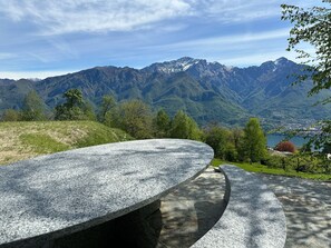 Una banca de pedra amb vista a un paisatge de muntanya, un llac i edificis a la distància.