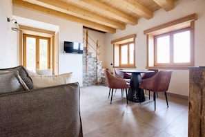Une pièce dotée d’un escalier en pierre, de poutres en bois, d’une table à manger avec des chaises et d’un téléviseur fixé au mur.
