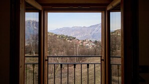 A view through a window with a wooden frame and a black metal railing, overlooking a town nestled among mountains. - Apartment in Luxury Chalet “Baita Treeb Breva” with Lake View & Wi-Fi - Civenna (Bellagio) (Bellagio)