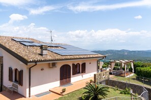 Uma villa com telhado em telhas, painéis solares, um pátio de pedra e vista para o campo.