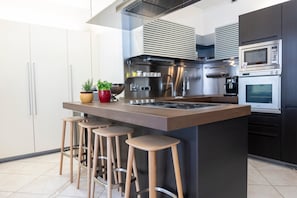 Uma cozinha moderna com ilha central, banquetas, eletrodomésticos de aço inoxidável e um vaso de planta.