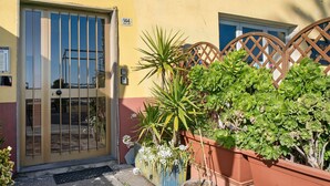 A yellow building with a metal gate, potted plants, and a number sign.