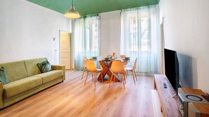 A living room with a green ceiling, a wooden dining table with chairs, a sofa, and a television.