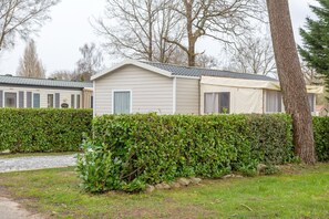 A mobile home with a small porch, a covered outdoor area, and a hedge in front.