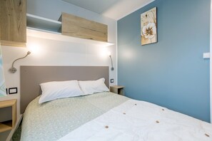 A bedroom with a bed, bedside tables, a wall-mounted shelf, and a painting.