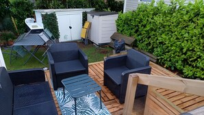 An outdoor patio area with wicker furniture, a patterned rug, and a wooden deck. - Mobile Home 'Tout Confort Bora Bora' with Shared Pool, Private Terrace and Private Garden (Pont-Aven)