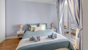 Un dormitorio con una cama, dos mesitas de noche, una ventana con cortinas y vistas al exterior.