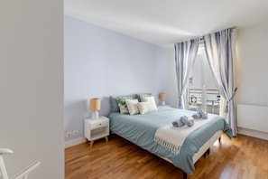 Un dormitorio con cama, mesitas de noche y ventana con cortinas.
