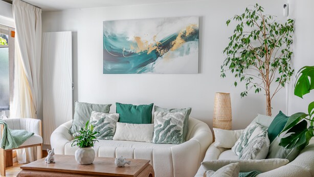 Una sala de estar moderna con un sofá blanco, cojines verdes, una mesa de centro de madera y un cuadro abstracto grande en la pared.