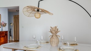 Un comedor con una mesa de mármol blanco, un centro de mesa de mimbre y sillas tapizadas en blanco.