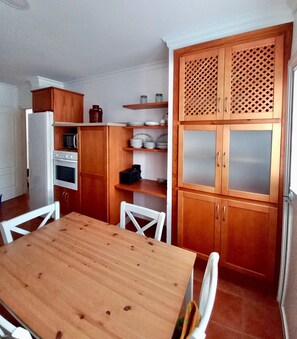 Keittiössä on puiset kaapit, mikroaaltouuni, uuni sekä ruokapöytä tuoleineen.