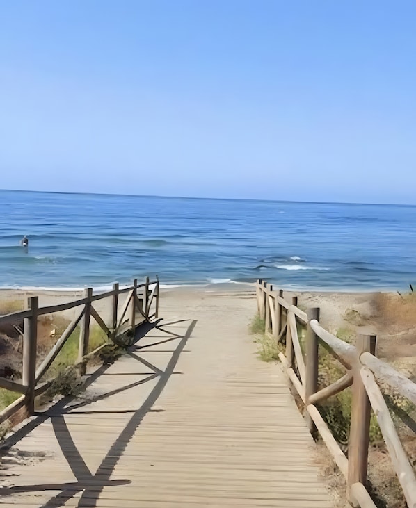 Una passerella in legno conduce a una spiaggia, con l'oceano sullo sfondo.