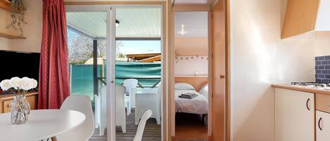 A room with a bed, a dining table with chairs, a TV, and a sliding door leading to an outdoor area with a table and chairs.