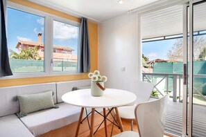 Un soggiorno moderno con un divano, un tavolino rotondo e una poltrona. Si vede una finestra con vista su edifici e un balcone.