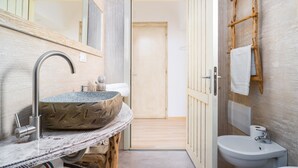 A bathroom with a stone sink, a wooden vanity, a mirror, a wooden ladder, and a toilet.