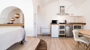A modern kitchen with built-in appliances, a dining area with a wooden table and chairs, and a bed with a white bedspread.