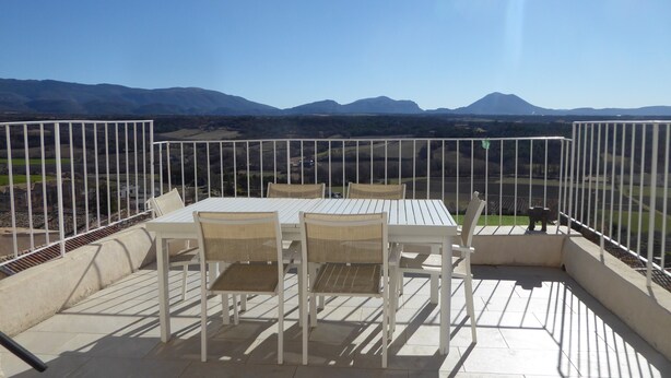 Une terrasse avec une table et des chaises, une vue sur des montagnes lointaines et un ciel dégagé.